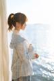 a woman standing in front of a window looking out at the ocean