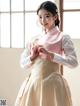 A woman in a pink and white hanbok poses for a picture.