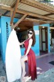 A woman in a red dress holding a surfboard.