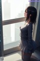 A woman standing in front of a window looking out at the city.