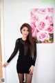 A woman in a black dress posing in front of a painting of pink roses.